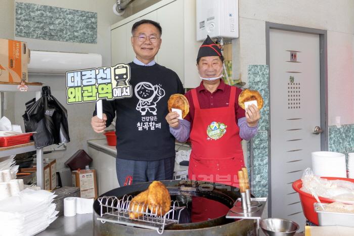 [크기변환]사진1김재욱 칠곡군수가 ‘대경선 왜관역에서’라는 문구가 적힌 팻말을 들고 웰빙왕호떡을 홍보하고 있다. 대경선을 타고 왜관역에 내려 호떡을 즐길 수 있다는 의미를 담은 촬영 장면..jpg